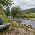 Ruhiger Bachlauf mit Kiesufer und einer geschlossenen Tasche am Wanderweg